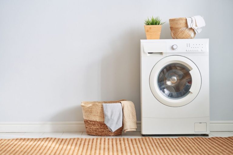 A washing machine and a laundry basket positioned in front of a clean white wall, emphasizing laundry care and maintenance.
