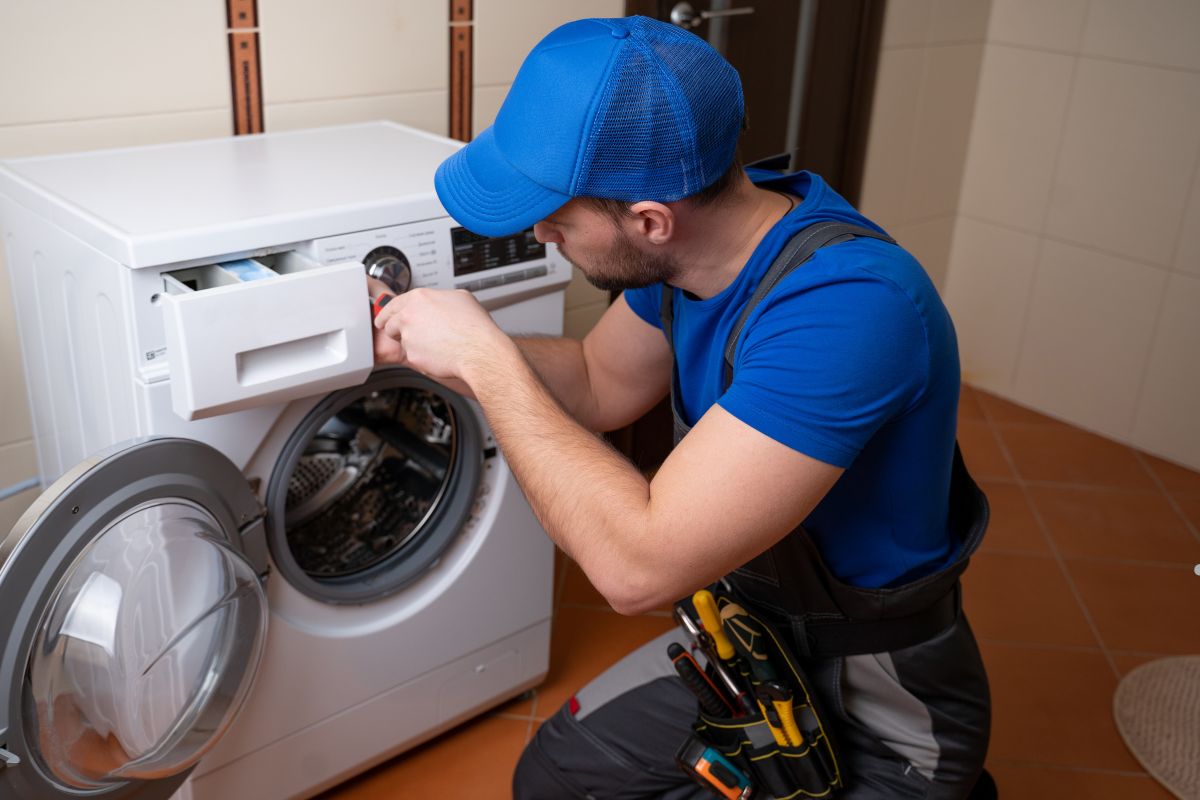  man in blue overalls repairs a washing machine, demonstrating the use of white vinegar for maintenance. 